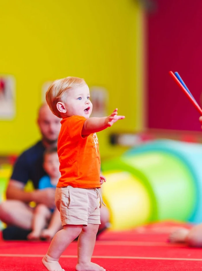 A child with their arm raised, happily playing during a Balance & Beam class